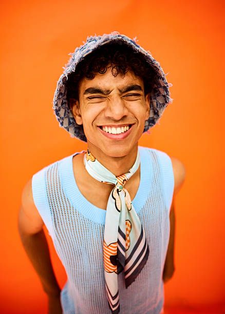 Young man wearing bucket hat and scarf on orange background feeling happy